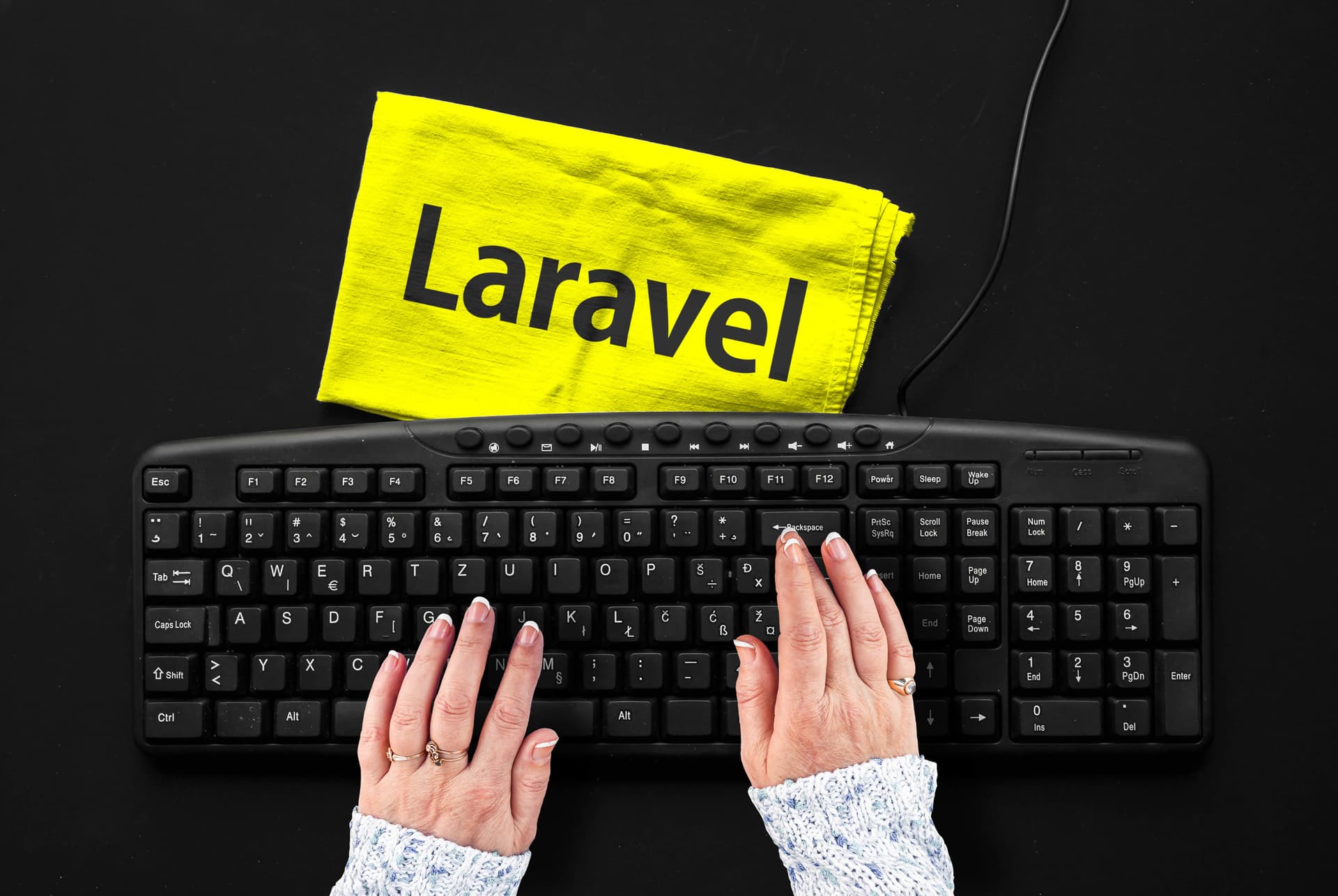 Hände tippen auf Tastatur, Laravel-Logo sichtbar.